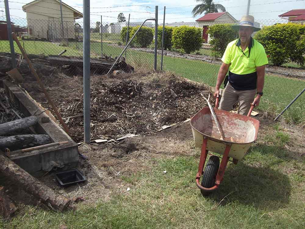 man in bright lime green shirt wheelbarrowing mulch