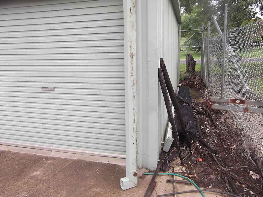narrow area between a fence and shed with grass litter and sticks